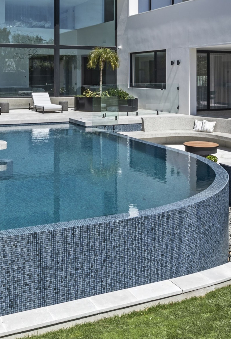 Modern pool by Bayside Pools with lounge chairs, plants, and a building in the background. Swimming pool equipment.